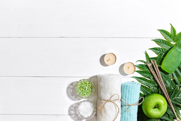 Spa products bath salts soap candles and towel flat lay on white wooden background top view