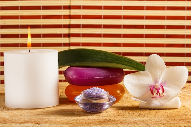 Spa products with burning candle, bowl with sea salt, soap and white orchid flower on wooden background.