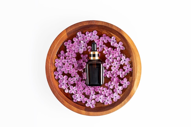 Spa relax composition with fresh sprig of lilac and bottle on wooden bowl white background Wellness home skin care and spa relax treatment concept