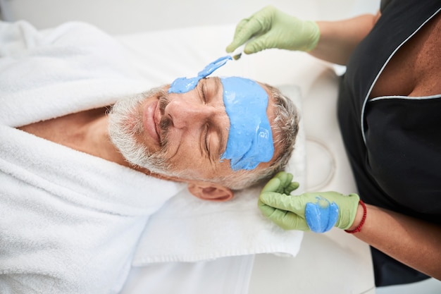 a spa salon worker putting blue foam over an aging man face