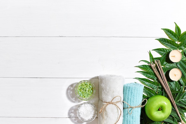 Spa still life with towel candles and green leaves on a white wooden surface