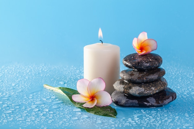 Spa stone pile with flowers and water drops on a blue wall