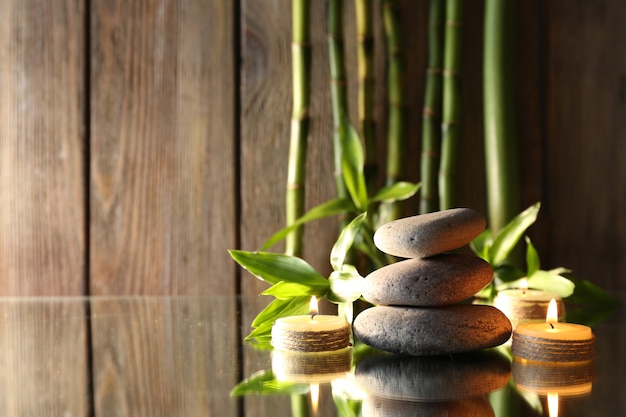 Spa stones candles and bamboo branches on mirror surface on wooden wall