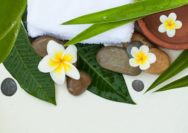 Spa or wellness background with white towels tropical leaves flowers and stones top view