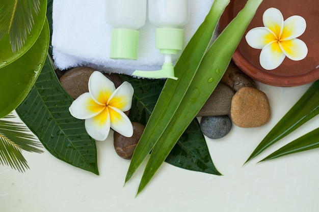 Spa or wellness background with white towels tropical leaves stones flowers body and face care tools and accessories on white background top view