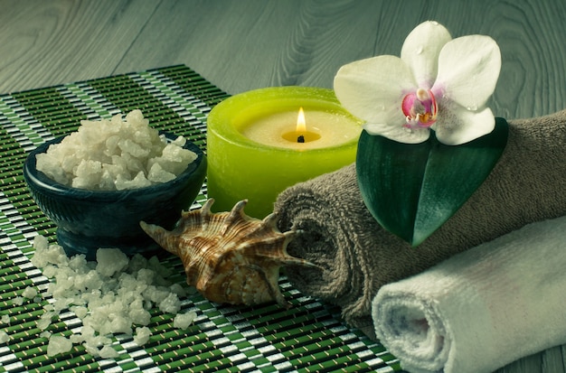 Spa and wellness setting with orchid flower, bowl with sea salt, seashell, candle and towels on bamboo napkin