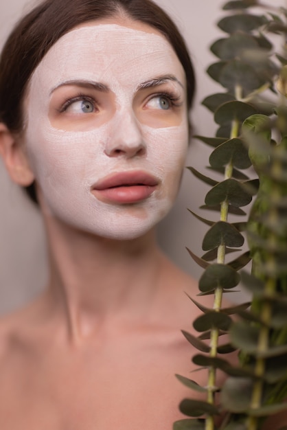 Spa Woman applying Facial clay Mask. Beauty Treatments. Close-up portrait of beautiful girl with a towel on her head applying facial mask.