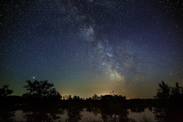 Space with stars in the night sky. The landscape with the river and trees is photographed on a long exposure.