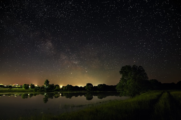 Space with stars in the night sky. The landscape with the river and trees is photographed on a long exposure.