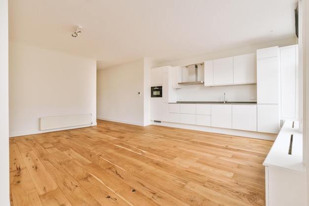 A spacious empty room with a corner kitchen on parquet floors