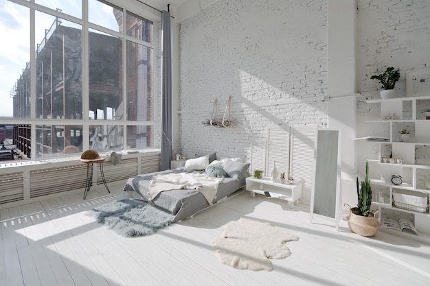 Spacious stylish modern trendy loft apartment in white and gray colors full of sunlight. brick wall, shelving, pallet bed and teepee-shaped children's house.