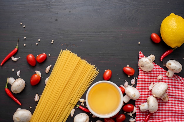 Spaghetti ingredients on black wooden desk, top view.