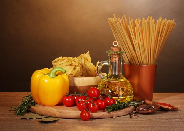 Photo spaghetti noodles in bowl jar of oil and vegetables on wooden table on brown background