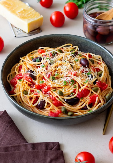 Spaghetti pasta Alla Puttanesca with capers Kalamata olives cheese tomatoes and anchovies Italian food