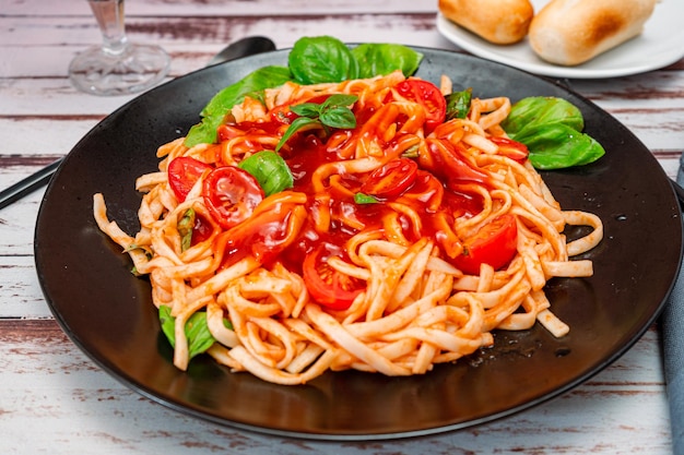 Spaghetti pasta with an exquisite tomato sauce with homemade basil leaves served on a black plate