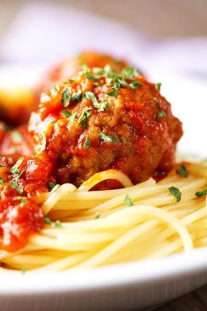 Spaghetti pasta with meatballs in tomato sauce and herbs on a white plate