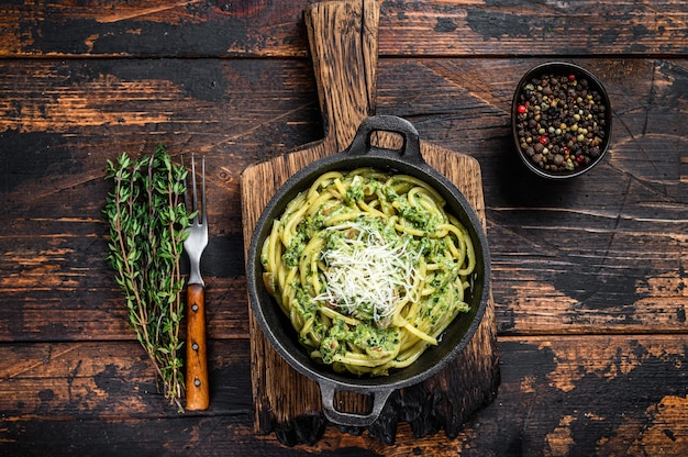 Spaghetti Pasta with pesto sauce, spinach and parmesan in a pan. Dark Wooden background. Top view.