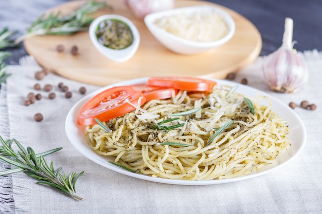 Spaghetti pasta with pesto sauce, tomatoes and cheese on a linen tablecloth.