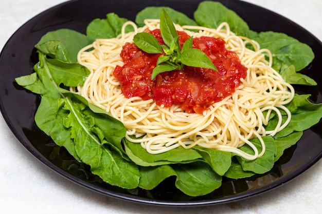 Spaghetti pasta with red sauce and arugula on black plate with white marble background