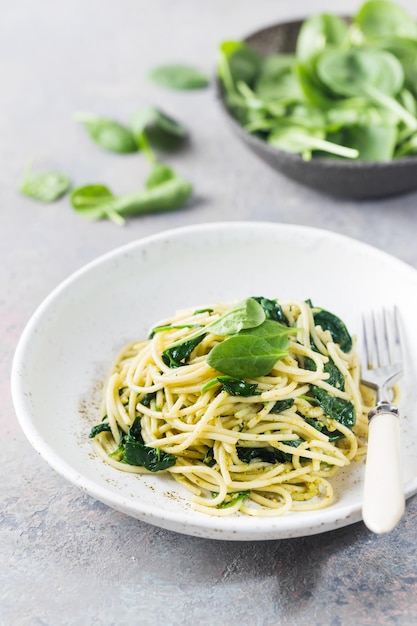 Photo spaghetti pasta with spinach and green pesto, in a white plate on gray stone background