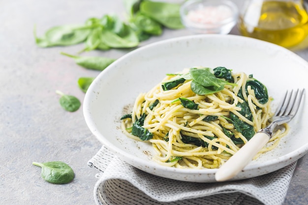 Photo spaghetti pasta with spinach and green pesto, in a white plate on gray stone background