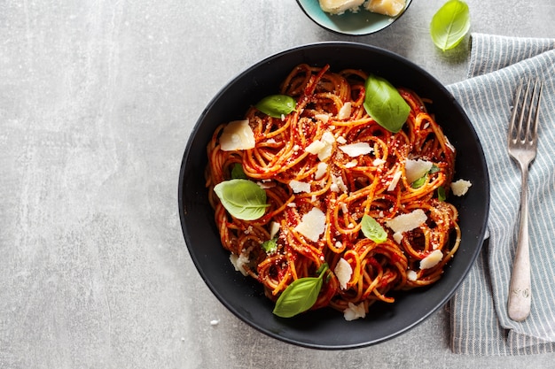 Spaghetti pasta with tomato sauce cheese and basil served in bowl on grey.