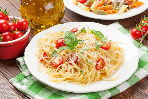 Spaghetti and penne pasta with tomatoes and basil on wooden table