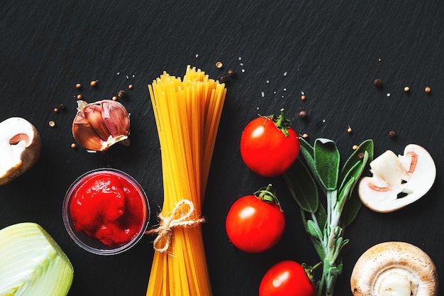 Spaghetti and various ingredients for cooking pasta. Black background, flat lay, copy space. Food background, Italian cuisine.