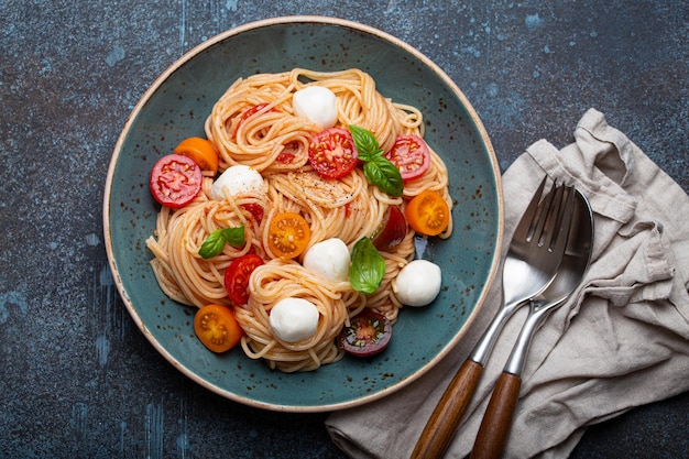 Spaghetti with mozzarella colourful cherry tomatoes fresh basil on ceramic plate