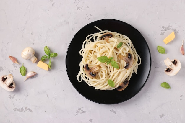 Spaghetti with mushrooms and basil on black plate on gray background