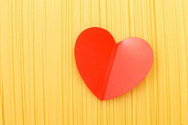 Spaghetti yellow background with a red heart close raw pasta macro