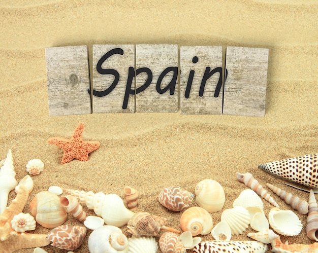 Spain on wooden board pieces with sea shells and sand