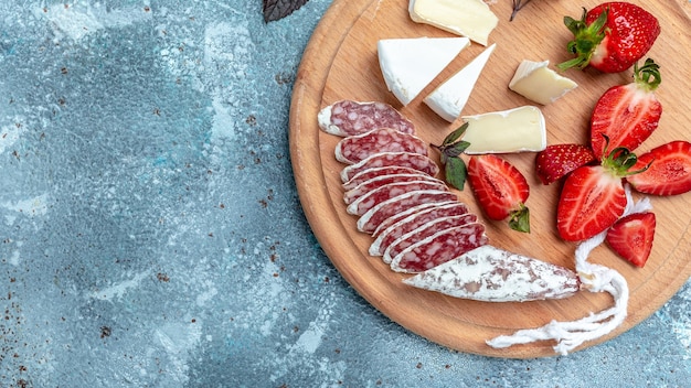 Photo spanish fuet salami wurst with camembert cheese, strawberries. long banner format. top view.