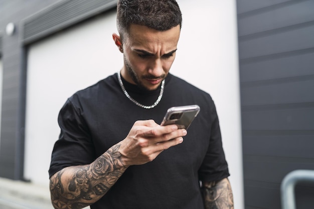 Spanish man with tattoos looking at his phone with a worried face