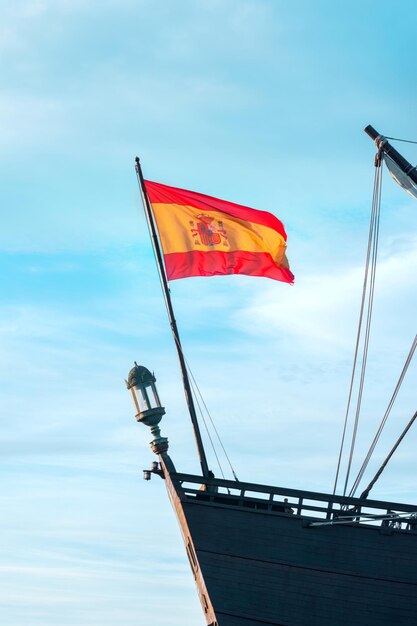 Spanish national flag on an ancient medieval frigate ship waving in the wind on blue sky background Patriotism symbol