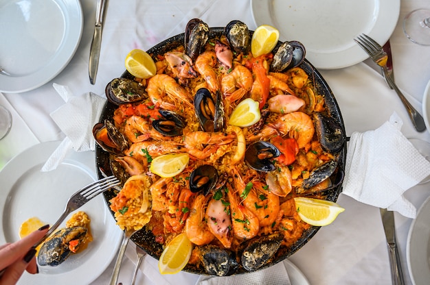 Spanish Seafood Paella Rice Dish with Fresh Shrimp, Scampi, mussels, squid, octopus and scallops Served in Pan.  The waiter puts a portion on the plate. Top view. Restaurant