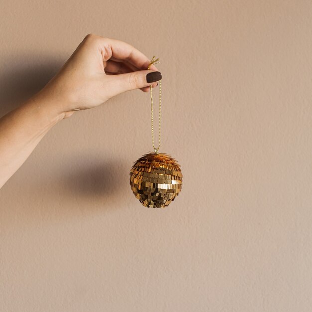 Sparkling glossy golden bauble in women hand on beige. Minimal Christmas holidays celebration decoration.