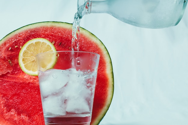 Sparkling water that is poured into a glass with ice and a slice of lemon. 
