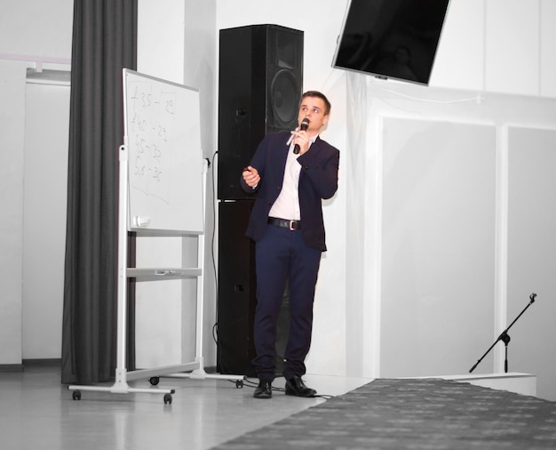 Speaker conducts the business of the conference standing in front of a large white screen on the stage in the conference room