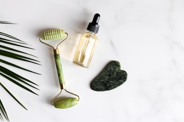 Special devices for Gua Sha Jade face roller stone for massage and essential oil on marble table