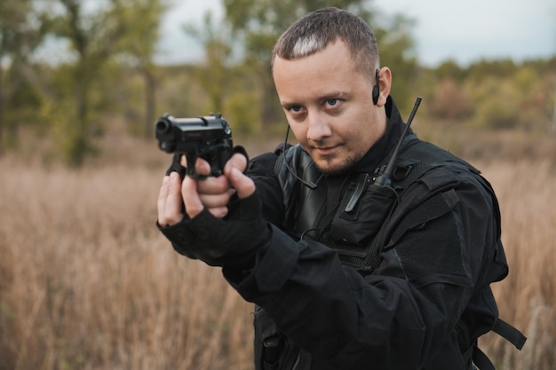 Special forces soldier in black uniform aiming a pistol