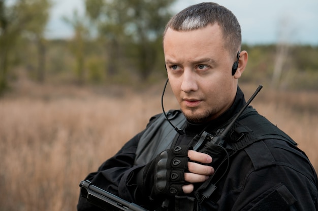 Special forces soldier in black uniform with a pistol speaking on the radio