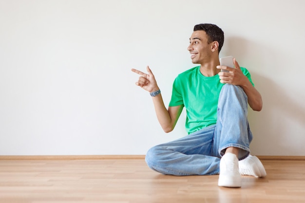 Special mobile offer Excited man pointing aside at free space holding cellphone over light wall background