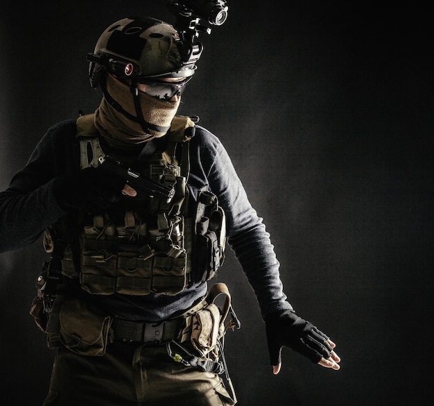 Special operations fighter in helmet with nightvision thermal imaging device load carrier carefully moving with caution in darkness holding hand on pistol ready for fight during dangerous mission