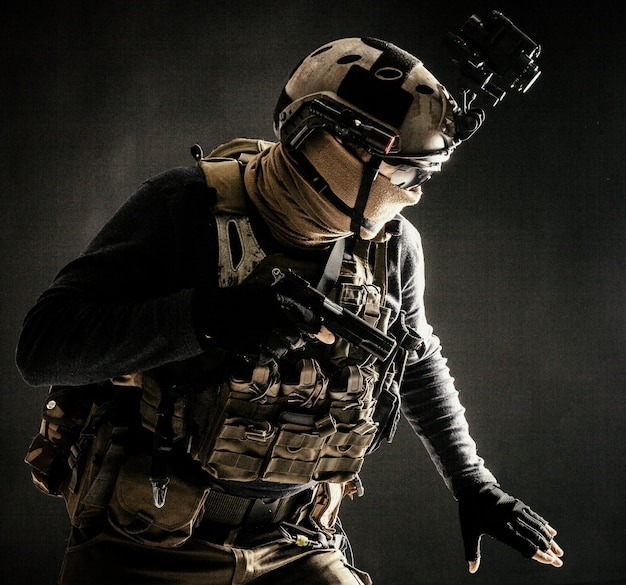 Special operations fighter in helmet with nightvision thermal imaging device load carrier carefully moving with caution in darkness holding hand on pistol ready for fight during dangerous mission