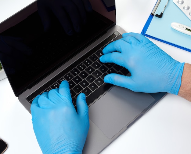 Specialist doctor in blue latex medical gloves working on a laptop, concept of remote maintenance