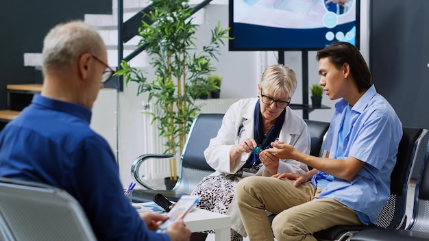 Photo specialist taking patient insulin level test using glucometer instrument in hospital reception. elderly doctor doing diabetes examination to measure glucose from blood sample. medicine service support