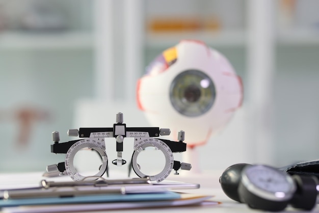 Spectacles used for eyesight test on table against blurred realistic eye model professional