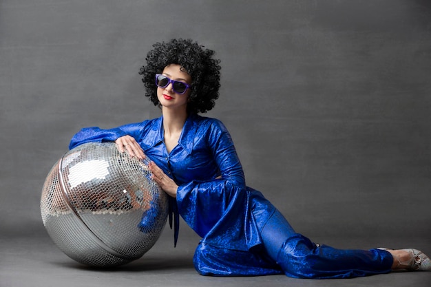 Spectacular Woman in a sparkly flared suit and afro wig poses with a disco ball