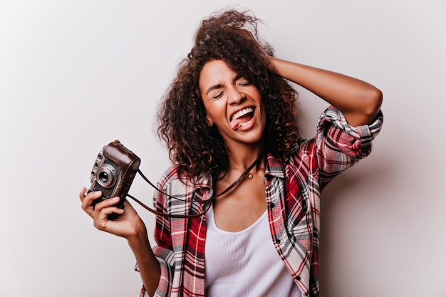 Spectacular young woman touching her hair and making funny faces Positive girl with camera having fun on white background